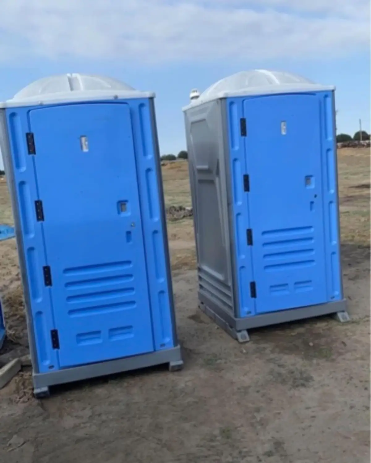 Two blue standard porta potties set on a dirt lot ready for a West Texas jobsite