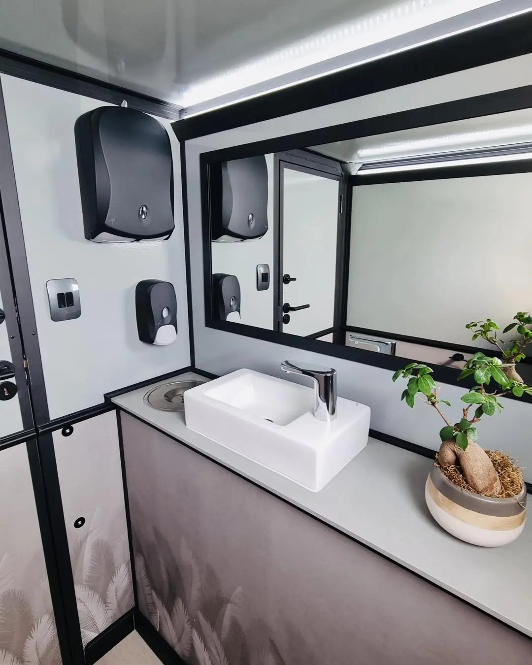 Vanity sink with soap dispenser and mirror inside a restroom trailer